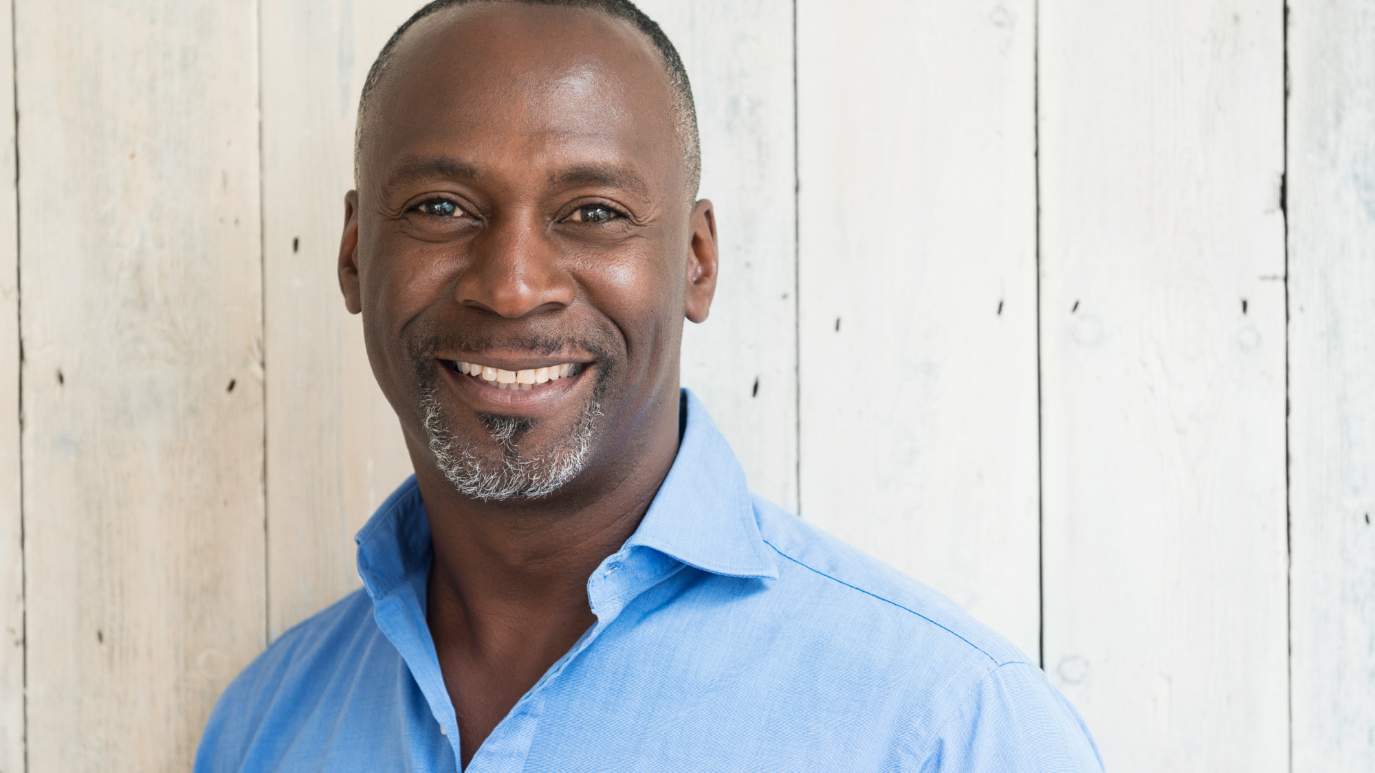 Similing african american man with light beard in blue shirt against a wooden wall