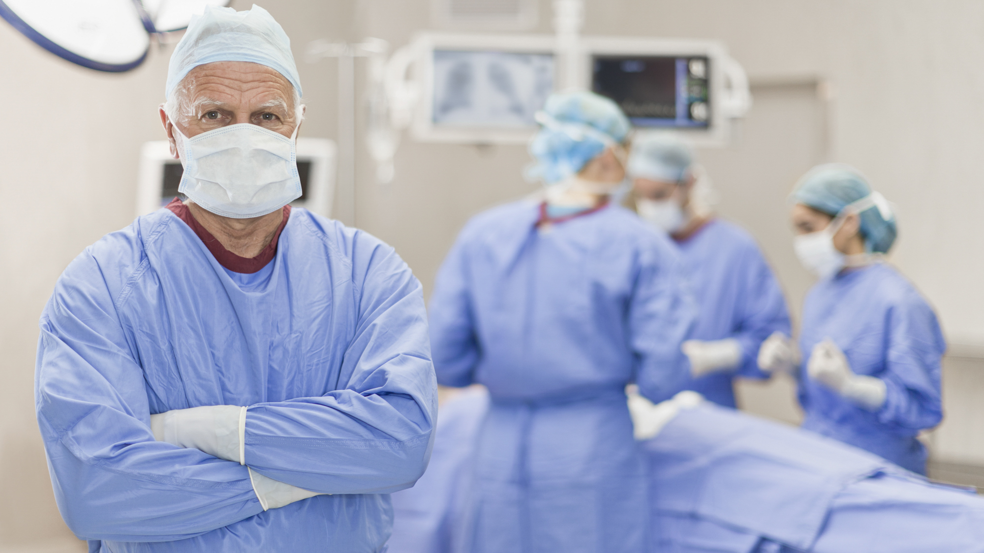 Masked surgeon in the OR with white hair showing and arms are crossed