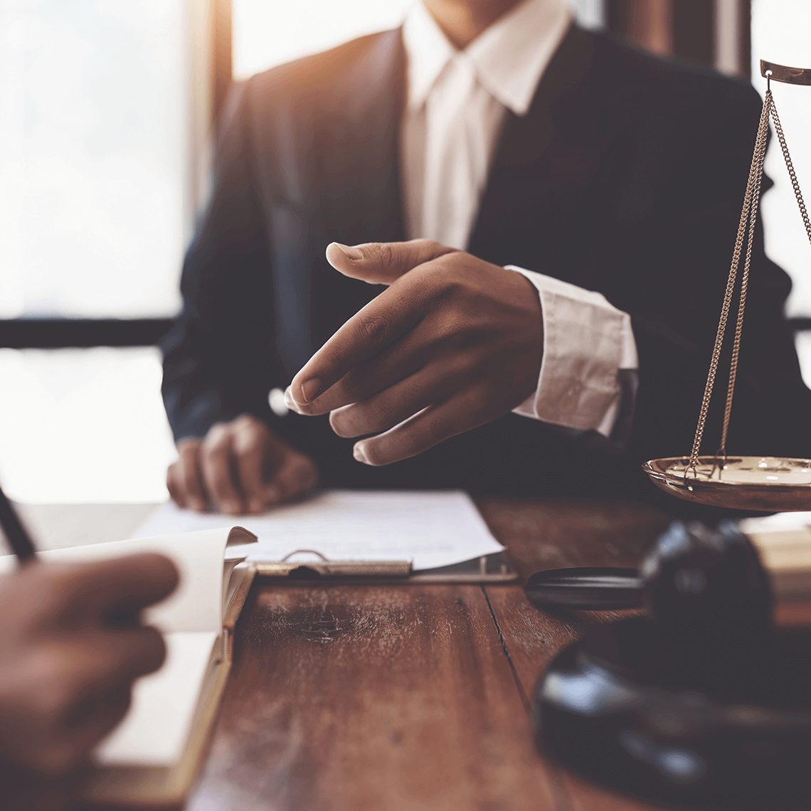 A close-up of a hand gesturing during a discussion, with legal documents and a gavel on a wooden table in a professional setting.